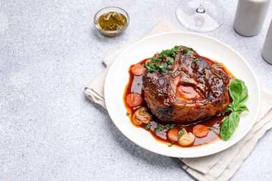 Photo of Tasty beef ossobuco with carrot, mushrooms and herbs on grey textured table, closeup. Space for text