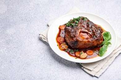 Photo of Tasty beef ossobuco with carrot, mushrooms and herbs on grey textured table, closeup. Space for text