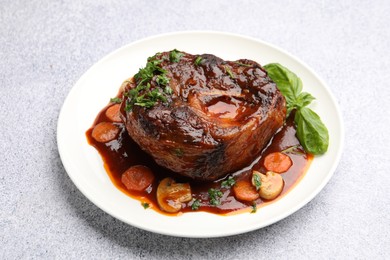 Photo of Tasty beef ossobuco with carrot, mushrooms and herbs on grey textured table, closeup