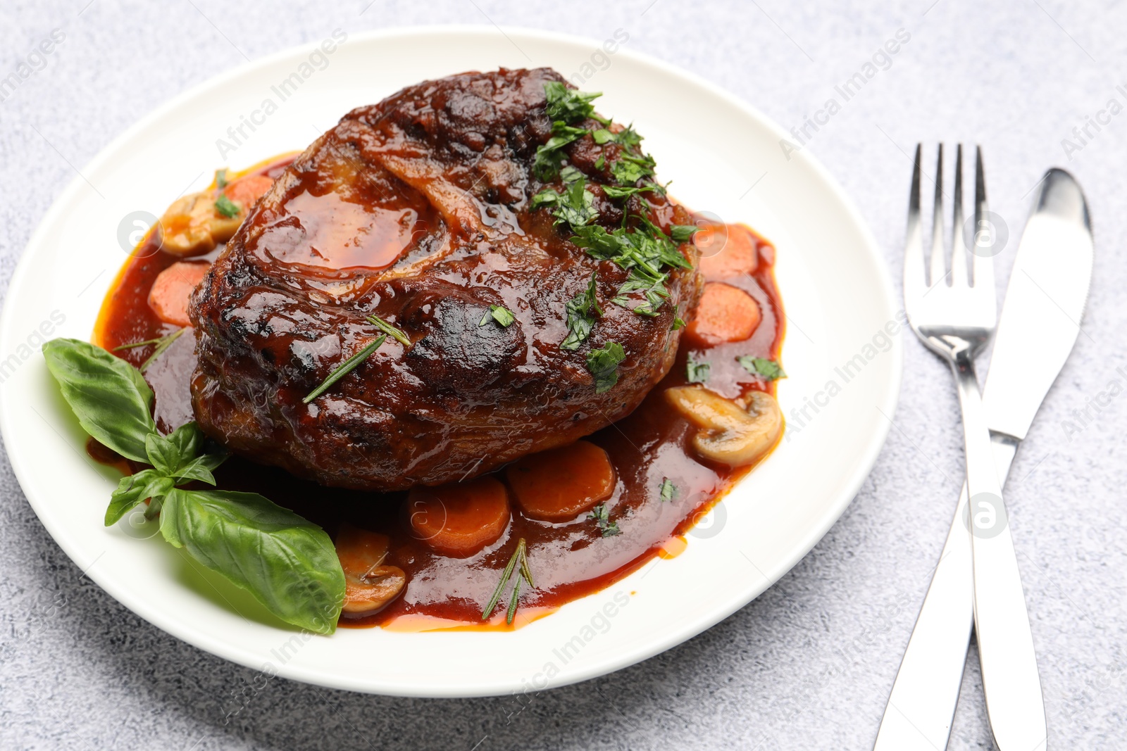 Tasty beef ossobuco with carrot, mushrooms and herbs on grey textured table, closeup Photo of Tasty beef ossobuco with carrot, mushrooms and herbs on grey textured table, closeup