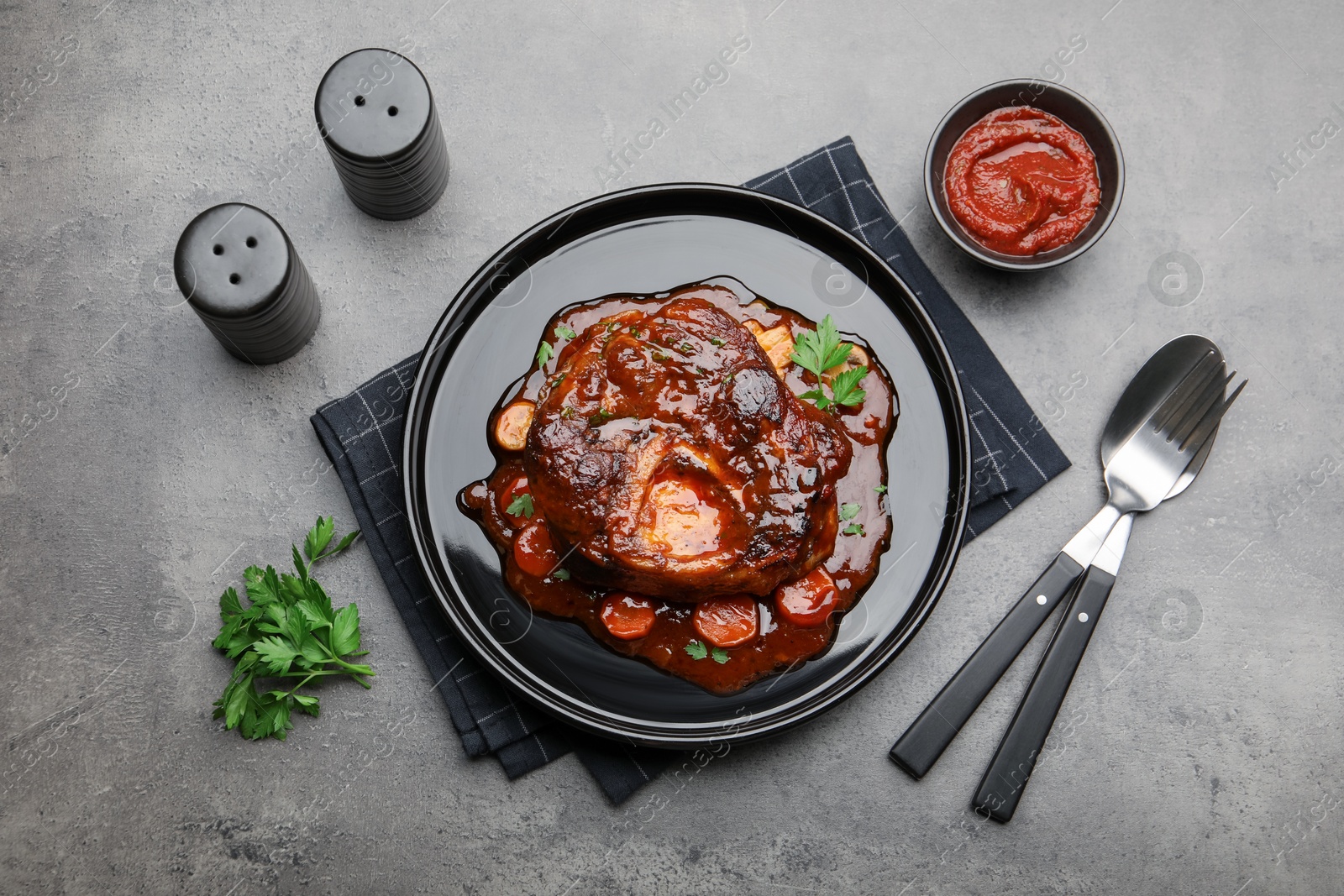 Tasty beef ossobuco with carrot, parsley and sauce served on grey textured table, flat lay Photo of Tasty beef ossobuco with carrot, parsley and sauce served on grey textured table, flat lay