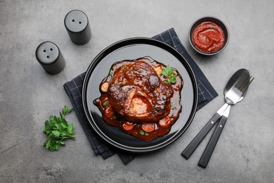 Photo of Tasty beef ossobuco with carrot, parsley and sauce served on grey textured table, flat lay