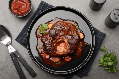 Photo of Tasty beef ossobuco with carrot, parsley and sauce served on grey textured table, flat lay