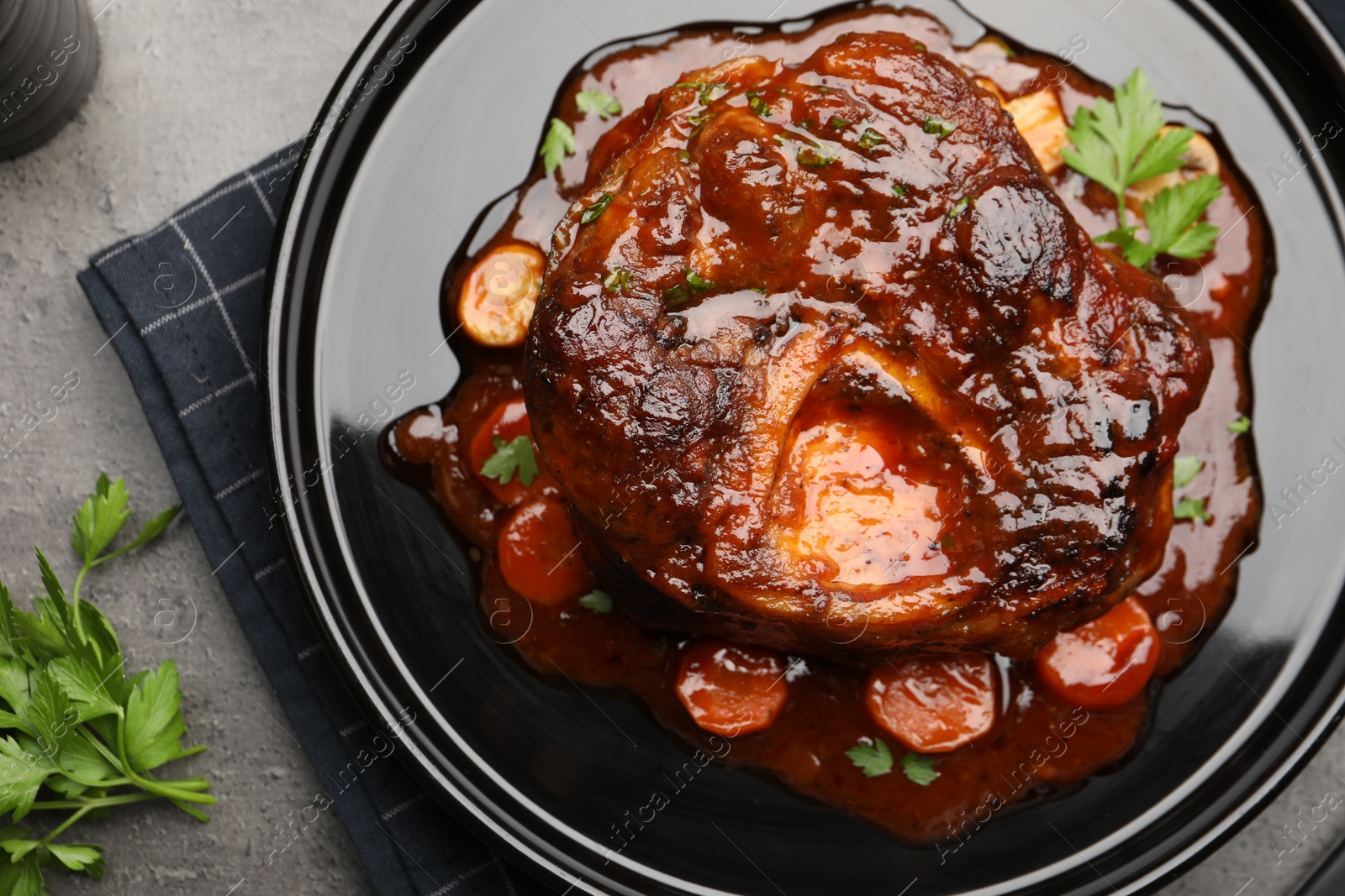 Tasty beef ossobuco with carrot, parsley and sauce on grey textured table, flat lay Photo of Tasty beef ossobuco with carrot, parsley and sauce on grey textured table, flat lay