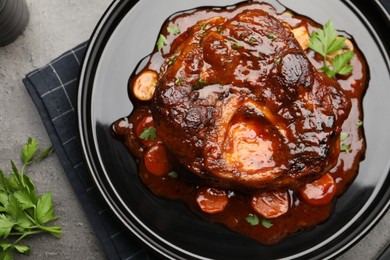Photo of Tasty beef ossobuco with carrot, parsley and sauce on grey textured table, flat lay
