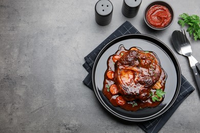 Photo of Tasty beef ossobuco with carrot, parsley and sauce served on grey textured table, flat lay. Space for text