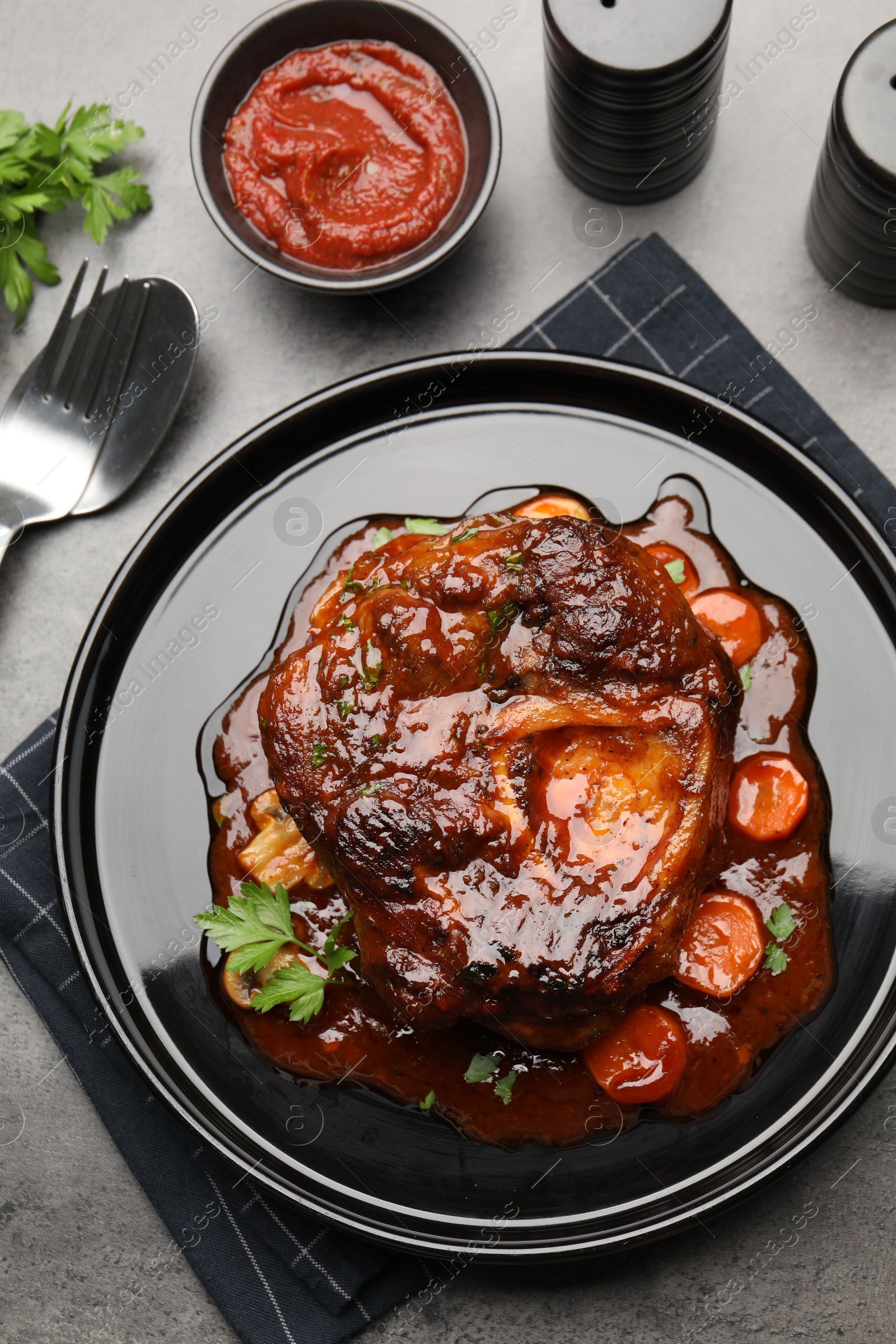 Tasty beef ossobuco with carrot, parsley and sauce served on grey textured table, flat lay Photo of Tasty beef ossobuco with carrot, parsley and sauce served on grey textured table, flat lay