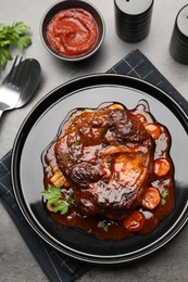 Photo of Tasty beef ossobuco with carrot, parsley and sauce served on grey textured table, flat lay