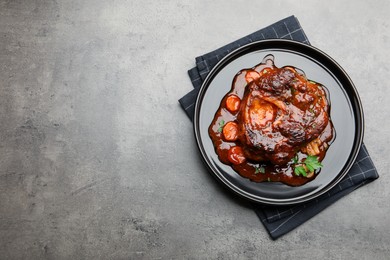 Photo of Tasty beef ossobuco with carrot, parsley and sauce on grey textured table, top view. Space for text