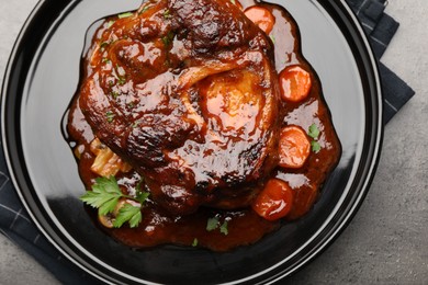 Photo of Tasty beef ossobuco with carrot, parsley and sauce on grey textured table, top view