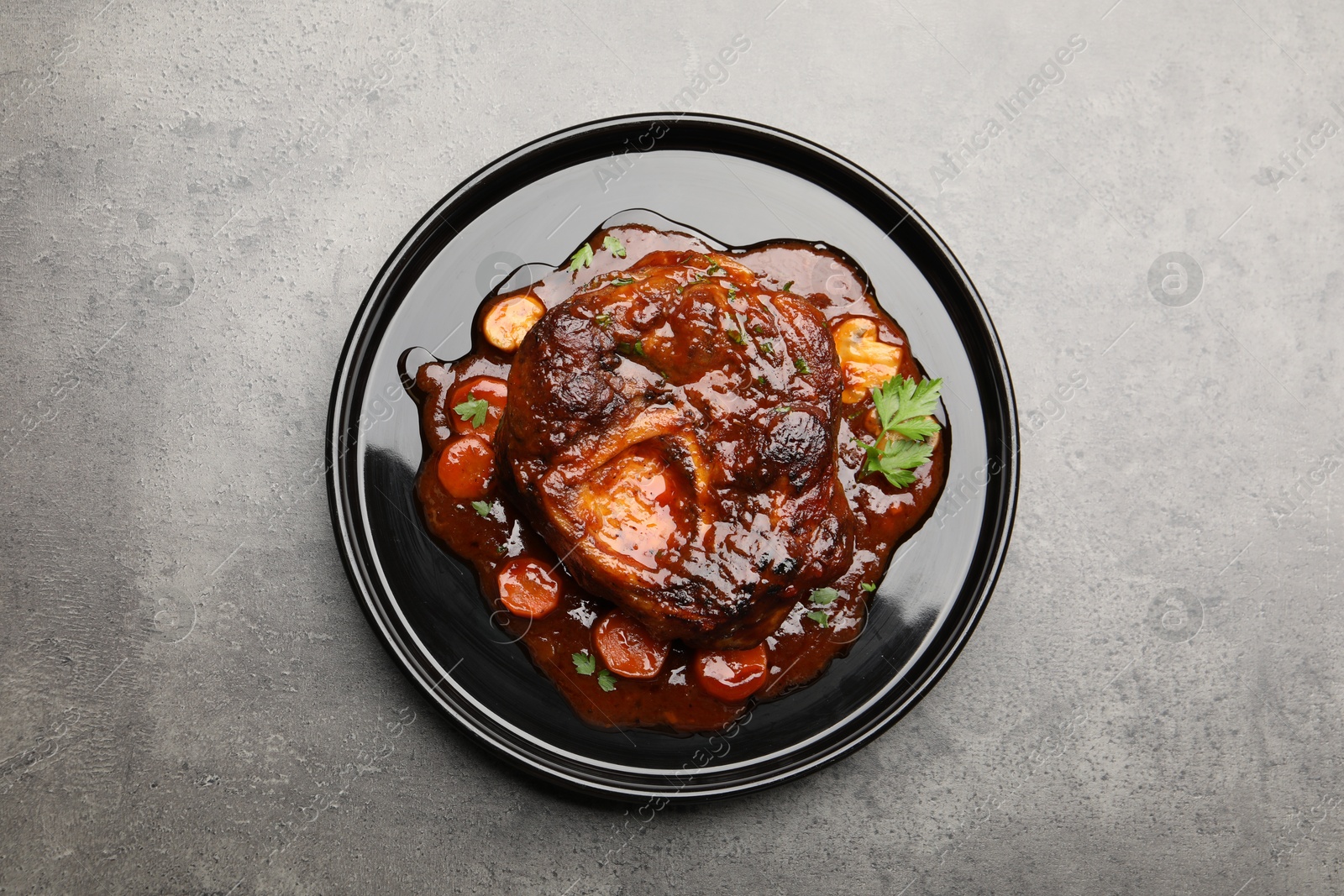 Tasty beef ossobuco with carrot, parsley and sauce on grey textured table, top view Photo of Tasty beef ossobuco with carrot, parsley and sauce on grey textured table, top view