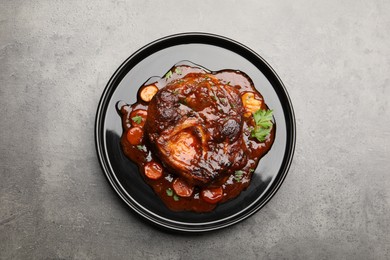 Photo of Tasty beef ossobuco with carrot, parsley and sauce on grey textured table, top view