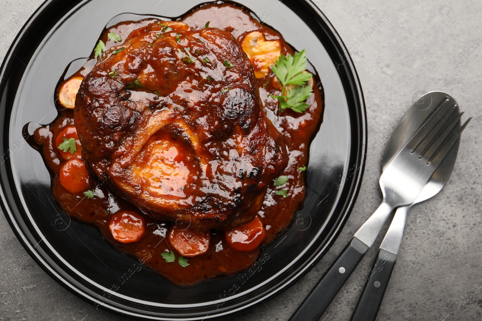 Tasty beef ossobuco with carrot, parsley and sauce on grey textured table, flat lay Photo of Tasty beef ossobuco with carrot, parsley and sauce on grey textured table, flat lay