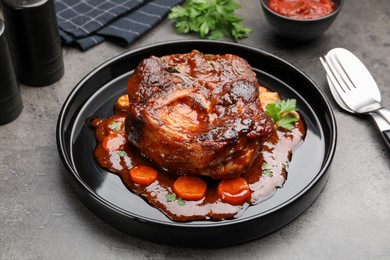 Photo of Tasty beef ossobuco with carrot, parsley and sauce on grey textured table, closeup