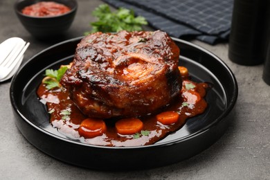 Photo of Tasty beef ossobuco with carrot, parsley and sauce on grey textured table, closeup