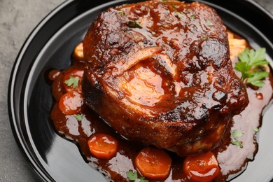 Photo of Tasty beef ossobuco with carrot, parsley and sauce on grey textured table, closeup