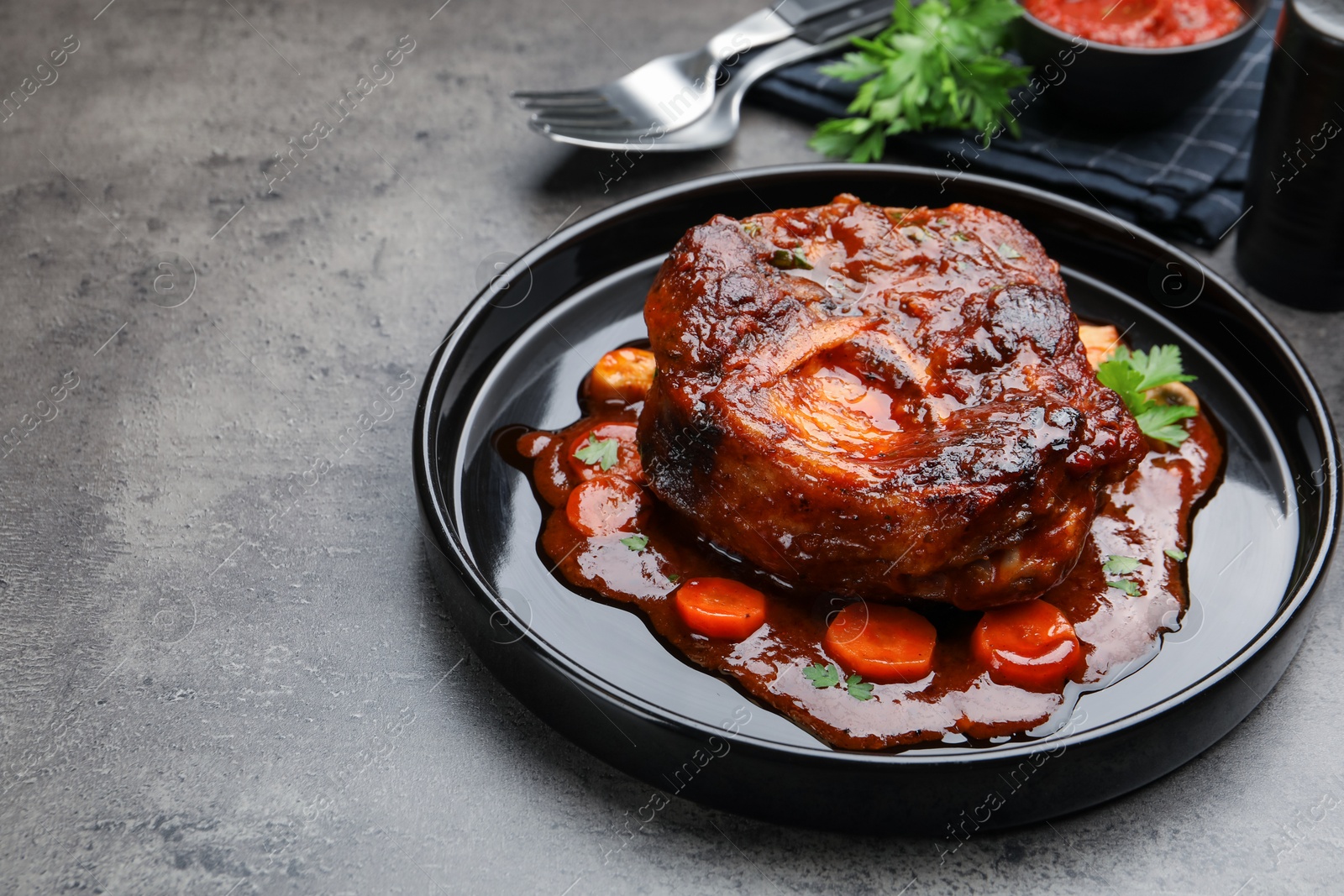 Tasty beef ossobuco with carrot, parsley and sauce on grey textured table, closeup Photo of Tasty beef ossobuco with carrot, parsley and sauce on grey textured table, closeup