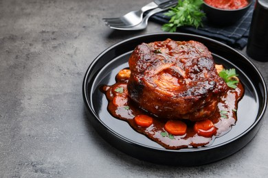 Photo of Tasty beef ossobuco with carrot, parsley and sauce on grey textured table, closeup