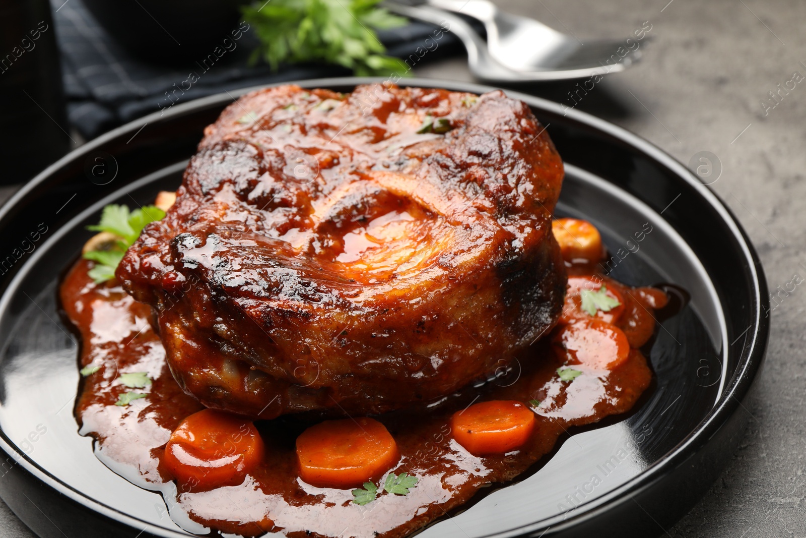 Tasty beef ossobuco with carrot, parsley and sauce on grey textured table, closeup Photo of Tasty beef ossobuco with carrot, parsley and sauce on grey textured table, closeup