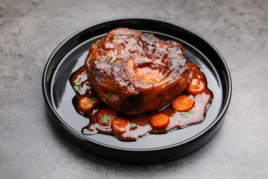 Photo of Tasty beef ossobuco with carrot, parsley and sauce on grey textured table, closeup