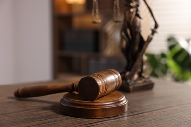 Photo of Judge's gavel and statue on wooden table in office, closeup