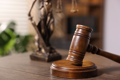 Photo of Judge's gavel and statue on wooden table in office, closeup