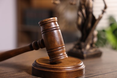 Photo of Judge's gavel and statue on wooden table in office, closeup