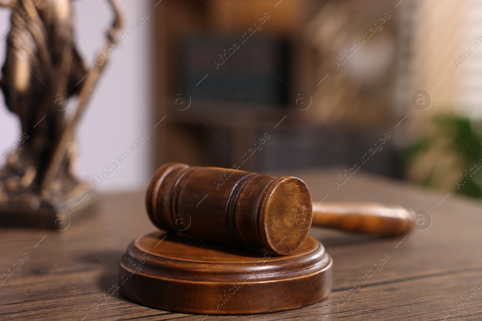 Photo of Judge's gavel and statue on wooden table in office, closeup