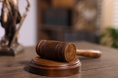 Photo of Judge's gavel and statue on wooden table in office, closeup