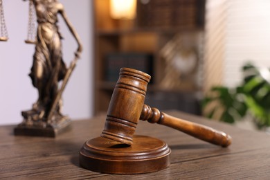 Photo of Judge's gavel and statue on wooden table in office, closeup