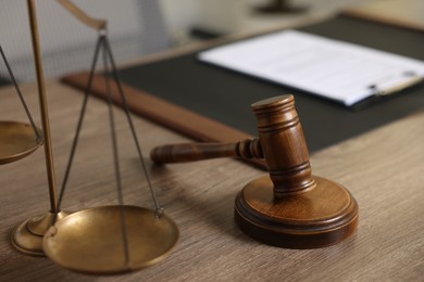 Photo of Judge's gavel and scales on wooden table in office, closeup