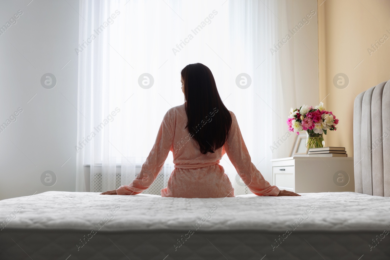Woman on bed with orthopedic mattress at home, back view Photo of Woman on bed with orthopedic mattress at home, back view