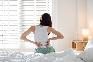 Photo of Woman stretching on bed with soft mattress at home, back view