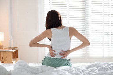 Photo of Woman stretching on bed with soft mattress at home, back view