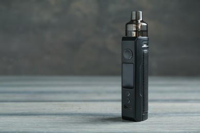 Photo of One electronic smoking device on wooden table against grey background, closeup. Space for text