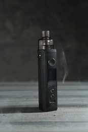 Photo of One electronic smoking device in smoke on wooden table against grey background, closeup