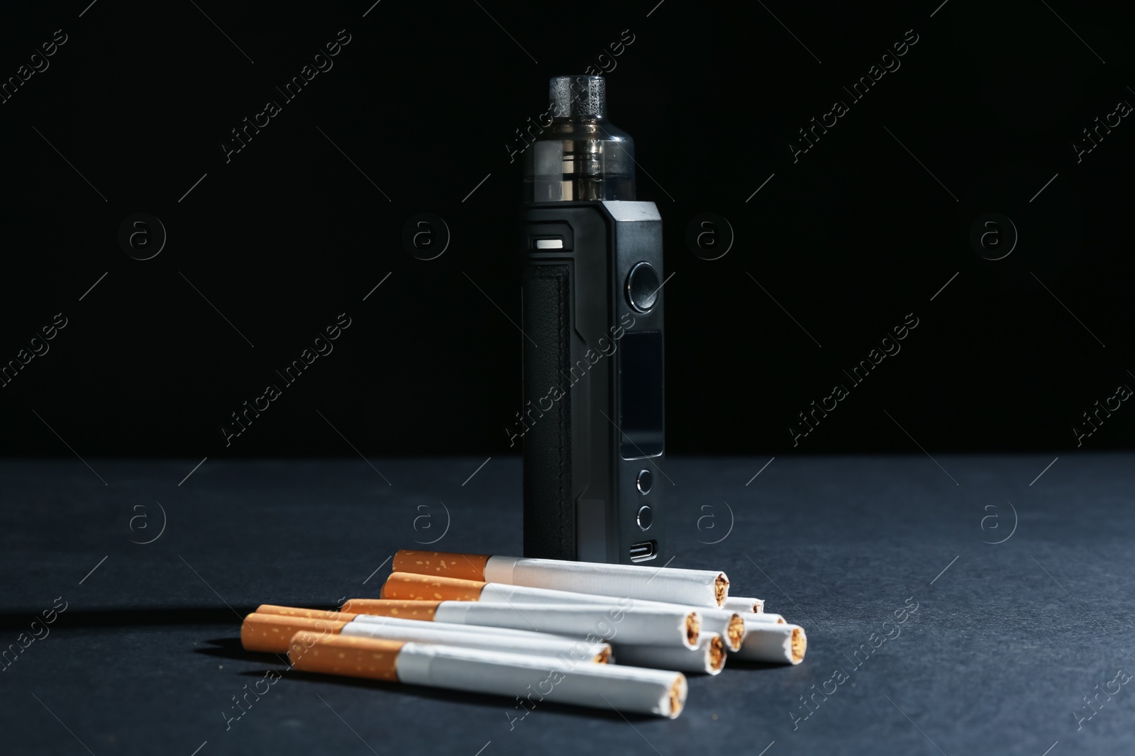Electronic smoking device and cigarettes on dark table against black background, closeup Photo of Electronic smoking device and cigarettes on dark table against black background, closeup