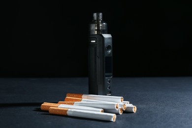 Photo of Electronic smoking device and cigarettes on dark table against black background, closeup