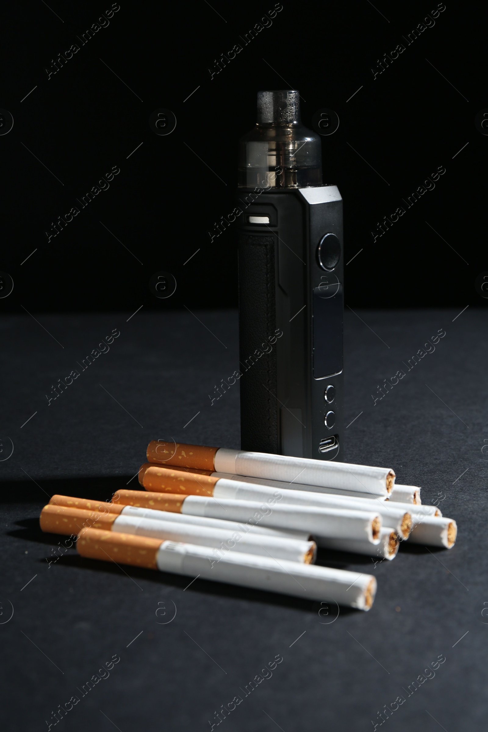 Electronic smoking device and cigarettes on dark table against black background, closeup Photo of Electronic smoking device and cigarettes on dark table against black background, closeup