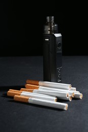 Photo of Electronic smoking device and cigarettes on dark table against black background, closeup