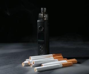 Photo of Electronic smoking device and cigarettes on dark table against black background, closeup