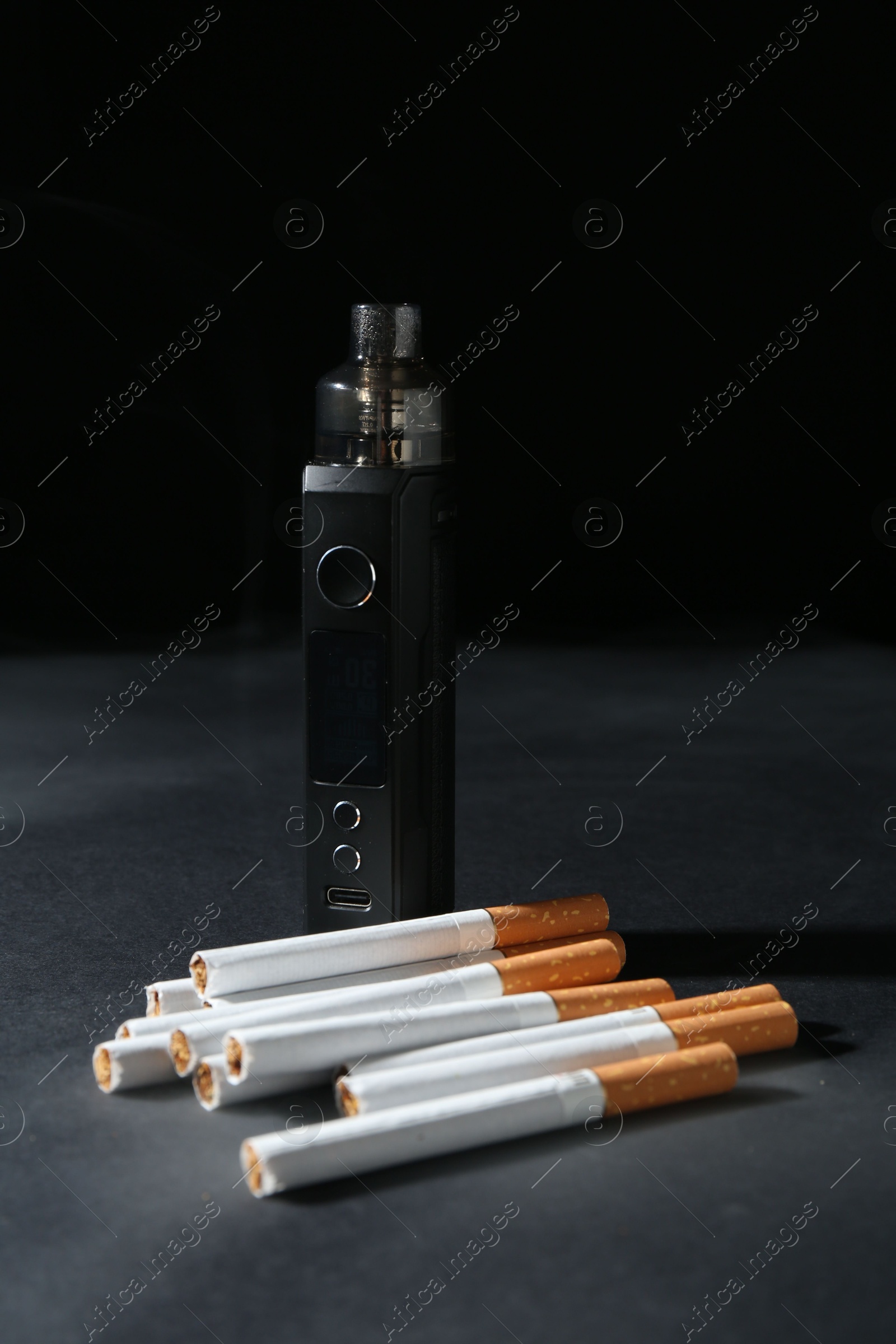 Electronic smoking device and cigarettes on dark table against black background, closeup Photo of Electronic smoking device and cigarettes on dark table against black background, closeup
