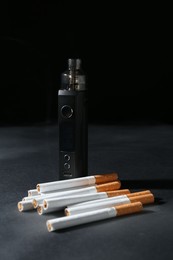 Photo of Electronic smoking device and cigarettes on dark table against black background, closeup