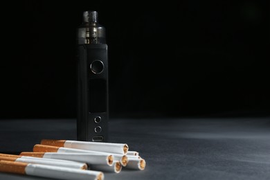 Photo of Electronic smoking device and cigarettes on dark table against black background, closeup. Space for text