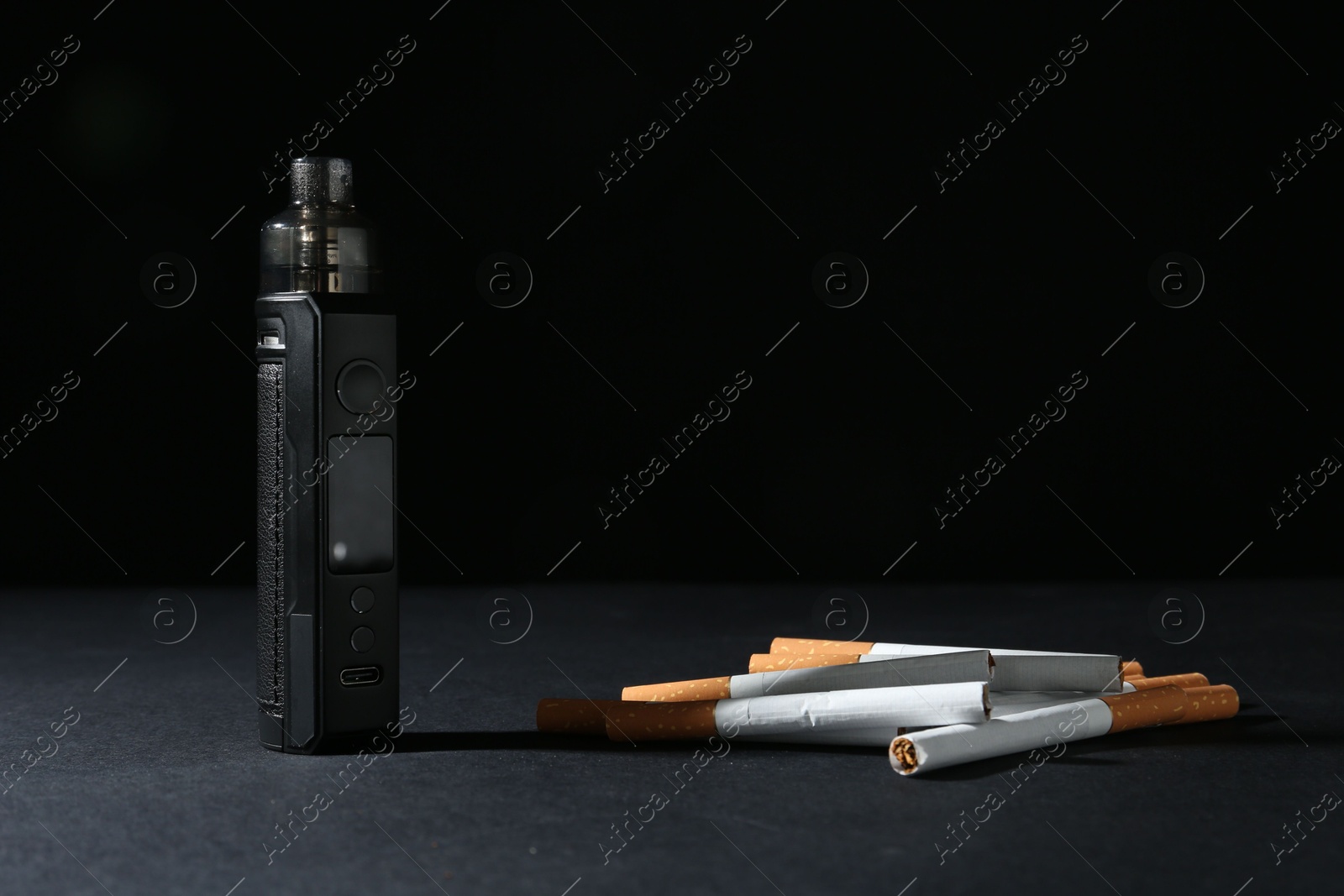 Electronic smoking device and cigarettes on dark table against black background, closeup Photo of Electronic smoking device and cigarettes on dark table against black background, closeup