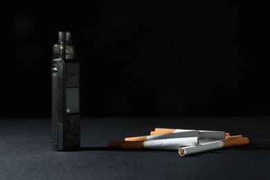 Photo of Electronic smoking device and cigarettes on dark table against black background, closeup