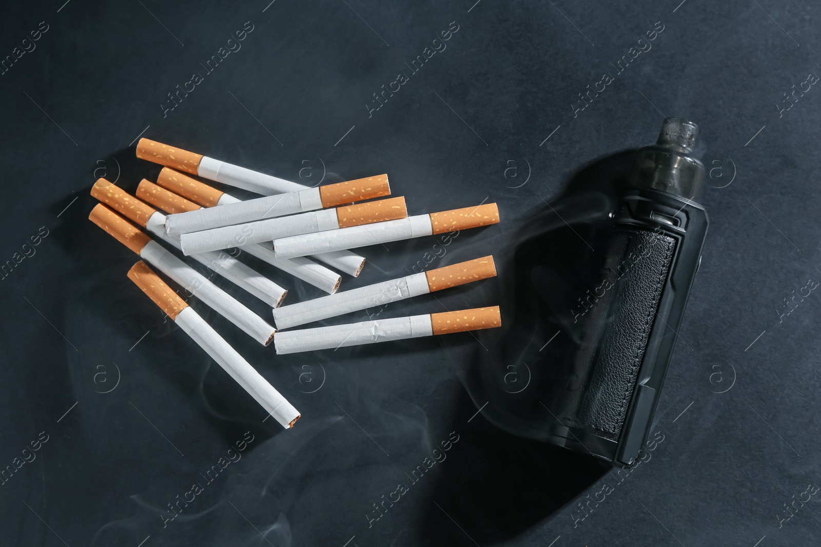 Electronic smoking device and cigarettes in smoke on dark table, flat lay Photo of Electronic smoking device and cigarettes in smoke on dark table, flat lay