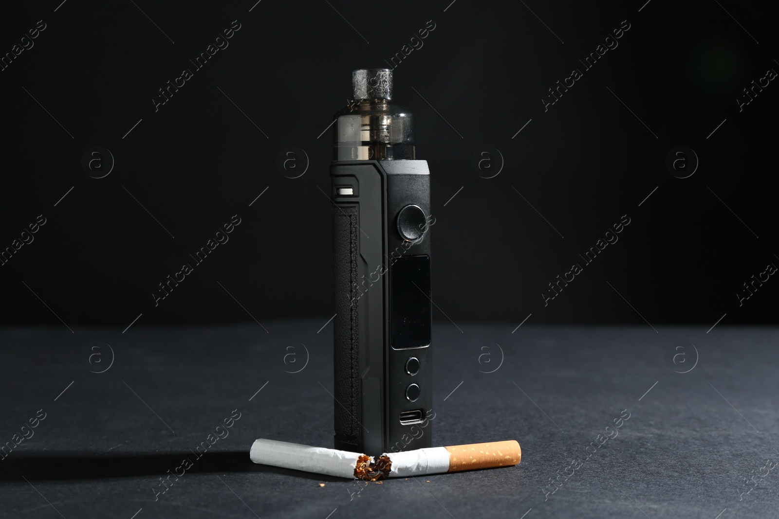 Electronic smoking device and broken cigarette on dark table against black background, closeup Photo of Electronic smoking device and broken cigarette on dark table against black background, closeup
