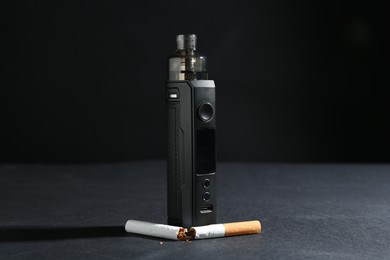 Photo of Electronic smoking device and broken cigarette on dark table against black background, closeup