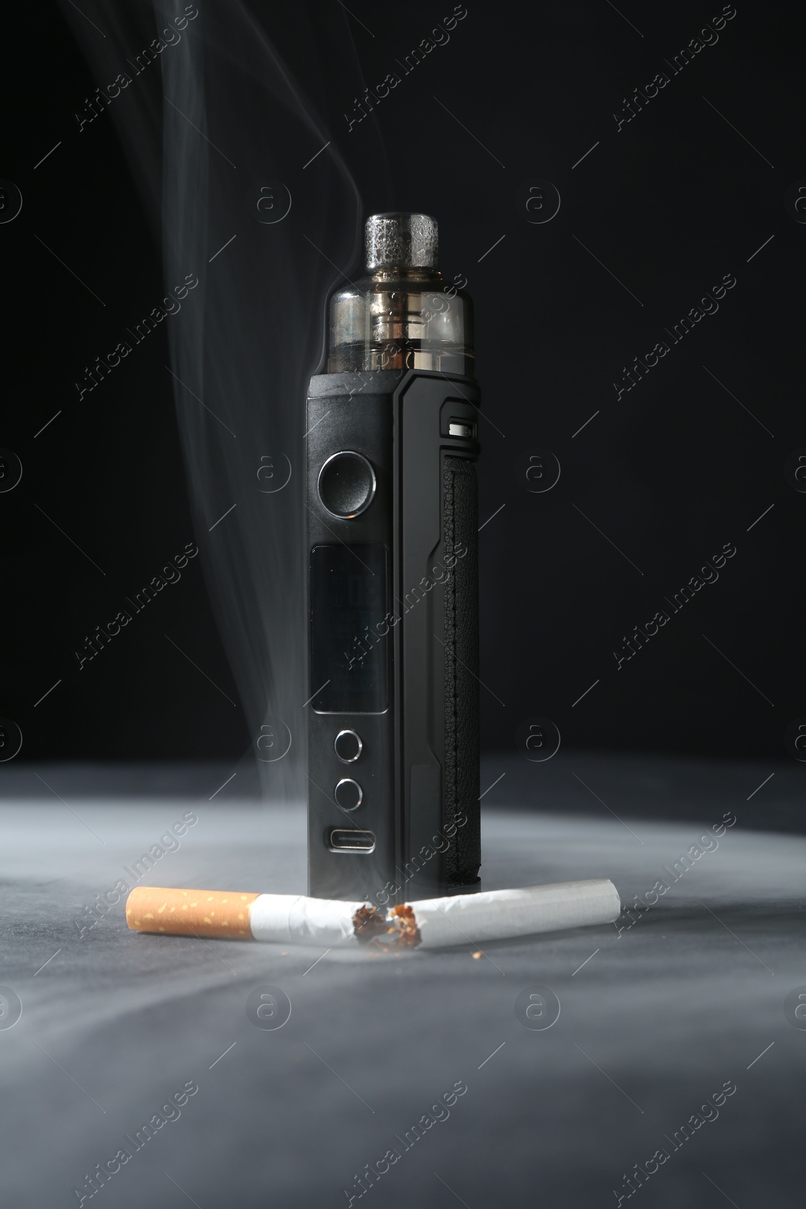 Electronic smoking device and broken cigarette in smoke on dark table against black background, closeup Photo of Electronic smoking device and broken cigarette in smoke on dark table against black background, closeup